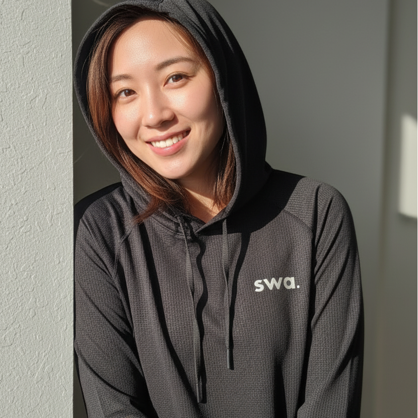 Person wearing a black swa sunhoodie with 'swa.' logo against a neutral wall