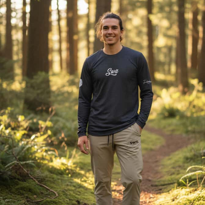 Man standing on a forest path wearing a black blue long-sleeve shirt and beige swa sweatpants.