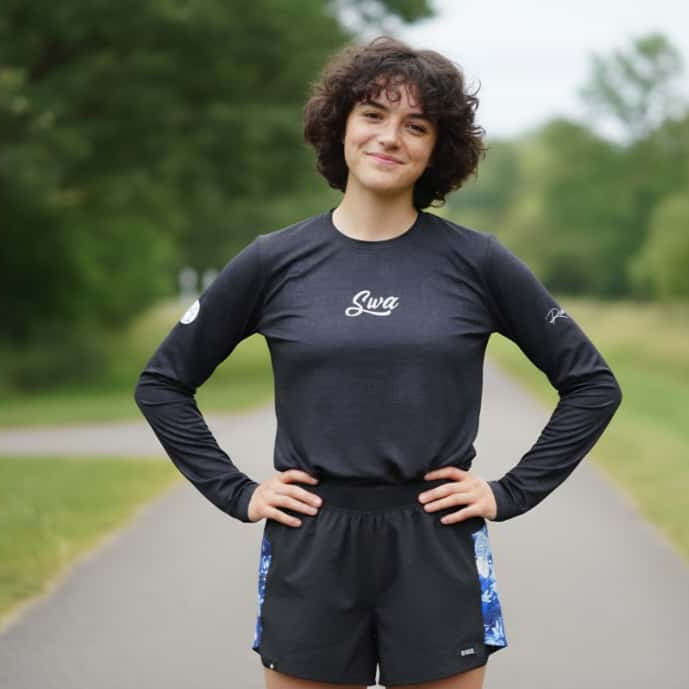 Person wearing a black long-sleeve shirt with a logo on a paved path in a park.