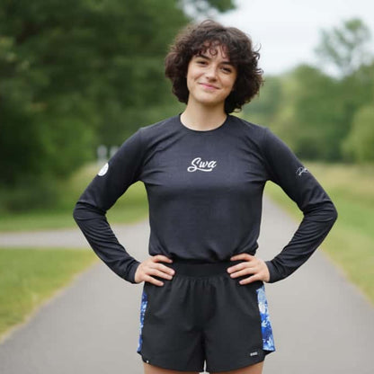 Person wearing a black long-sleeve shirt with a logo on a paved path in a park.