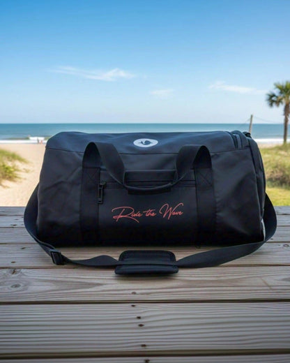 Black duffel bag with text on a wooden surface by the beach