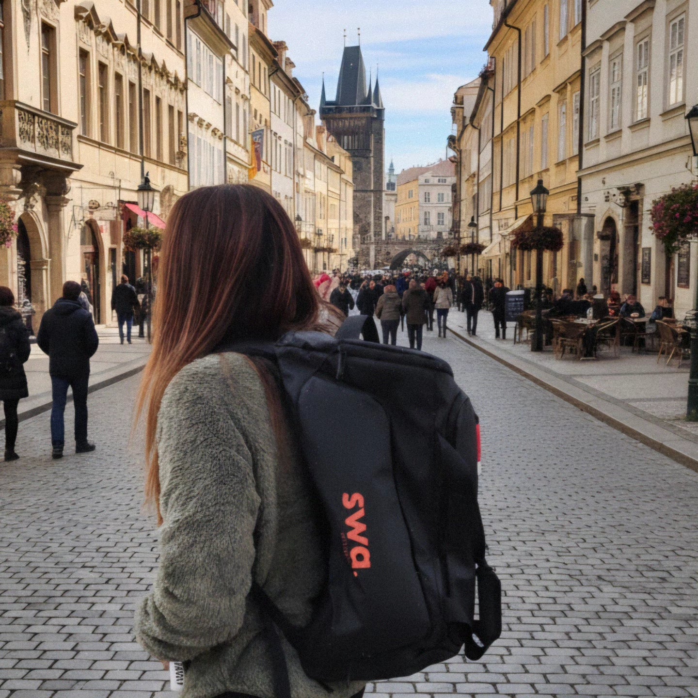 Person with a black backpack featuring 'swa' on a European street with historic architecture.