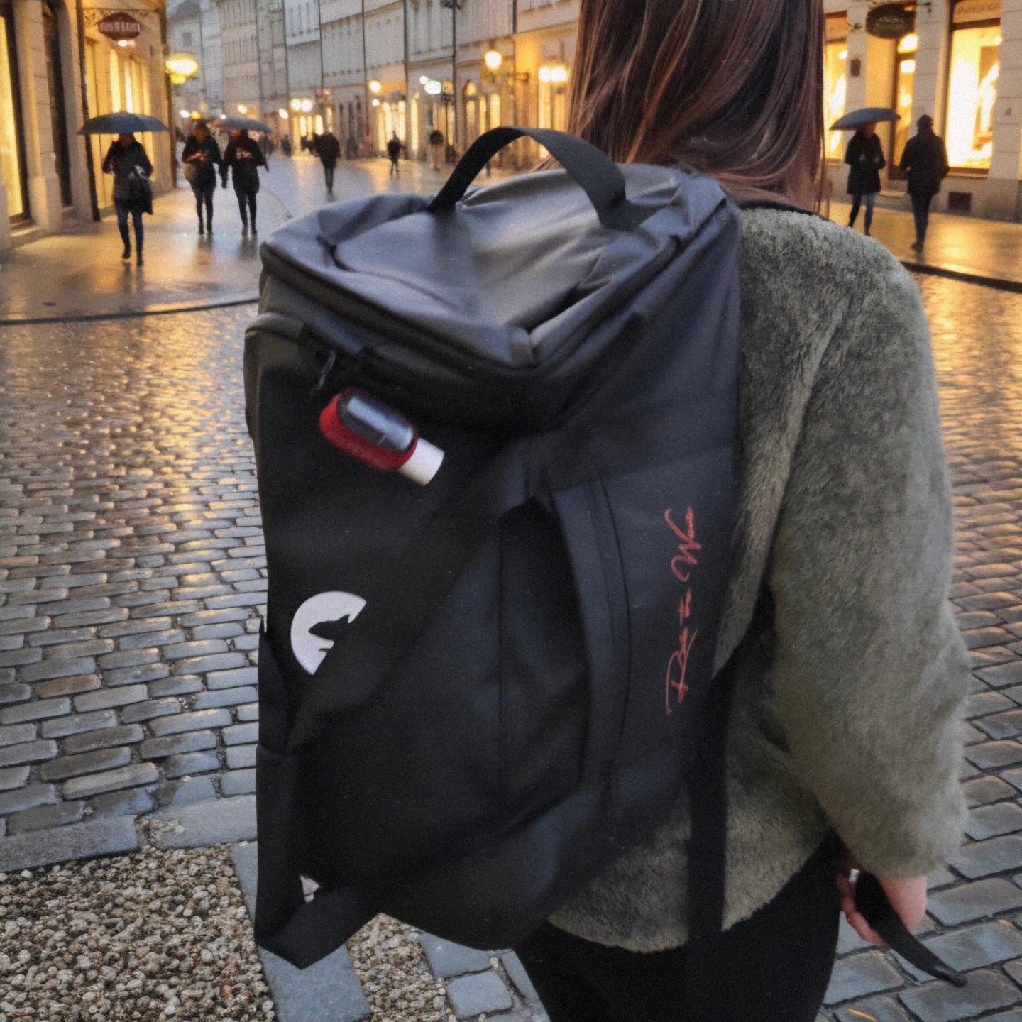 Person carrying a black backpack with visible branding on a city street.