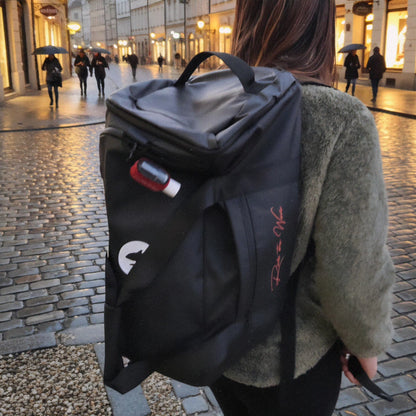 Person carrying a black backpack with visible branding on a city street.