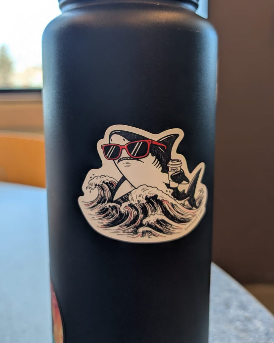 Black water bottle with a shark sticker design wearing sunglasses on a surface.